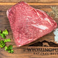 Raw arm roast beef on a wooden board with herbs and spices, branded 'Wyoming Pure Natural Beef'.